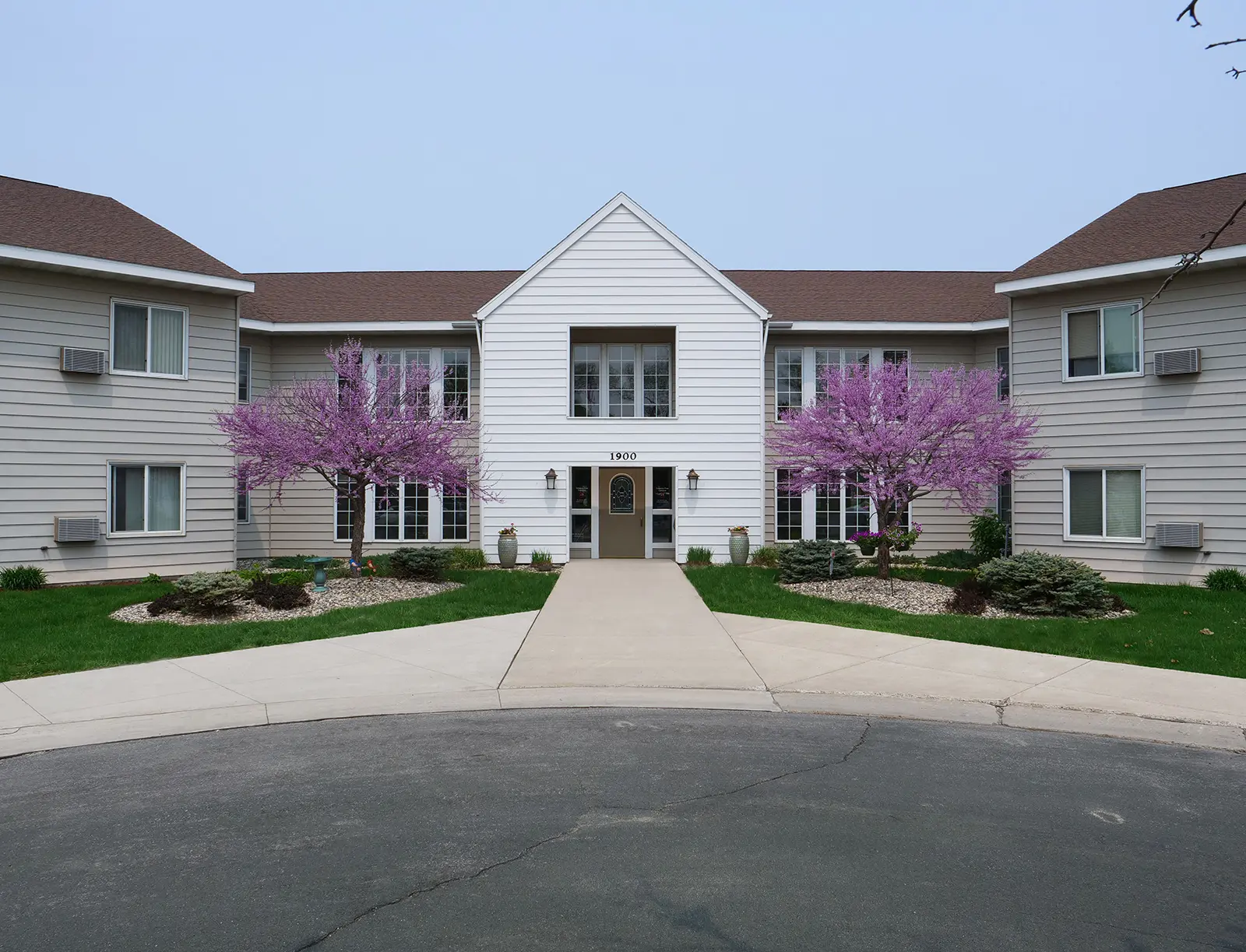 view of the entrance to orchard estates in between two trees with purple flower buds