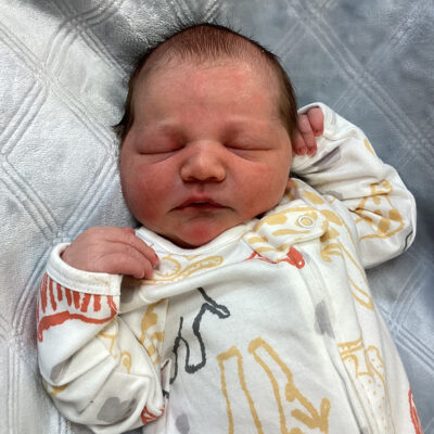 newborn baby in white onesie with animals